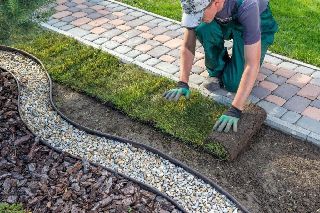 A man is laying down stones to form a garden path surrounded by greenery