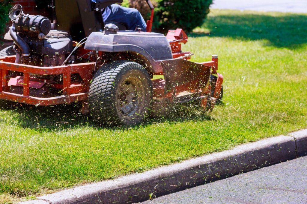 A man is mowing a green lawn with a push mower on a sunny day